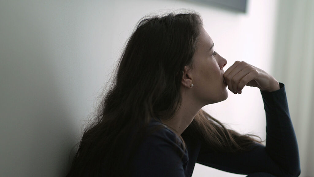 young woman leaning against her wall in a dimly lit room conteplating the dangers of opioid abuse