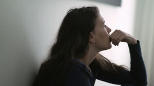 young woman leaning against her wall in a dimly lit room conteplating the dangers of opioid abuse