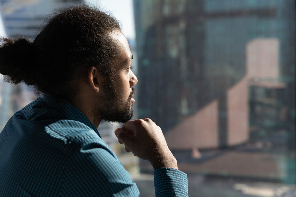 young man staring thoughtfully out a window recalling 10 tips for managing depression in your sobriety journey